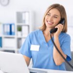 Nurse answering the phone, smiling, in front of laptop